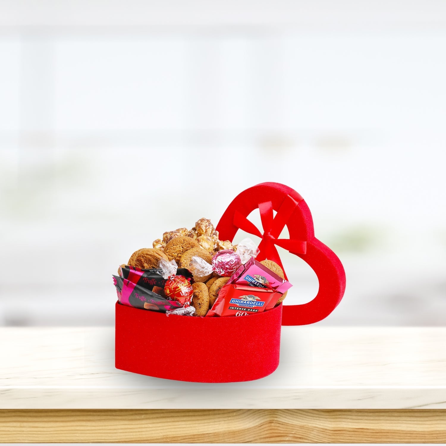 Red heart-shaped gift box filled with snacks on a wooden surface with a white background