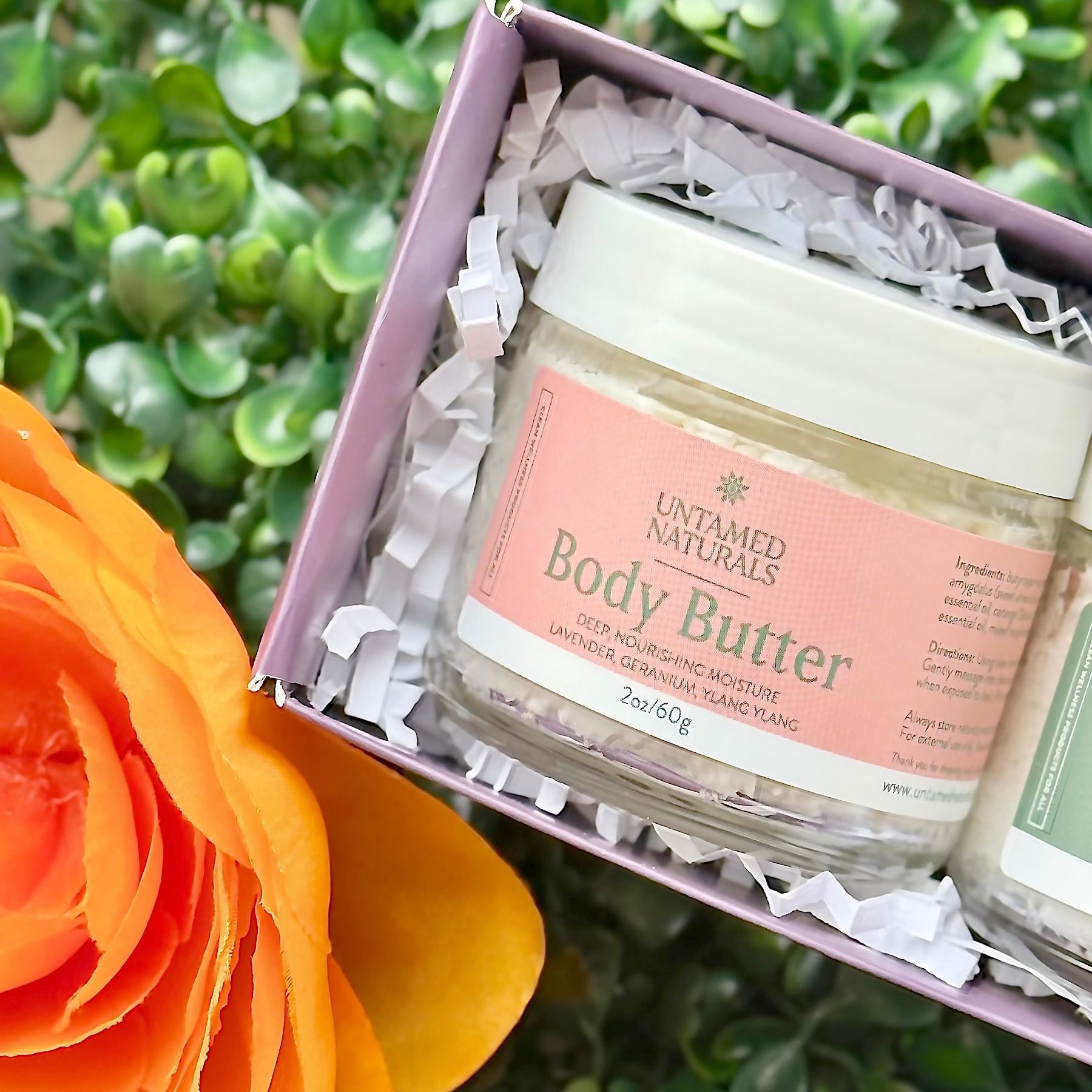 Jar of Untamed Naturals Body Butter in a box with an orange flower in the foreground.