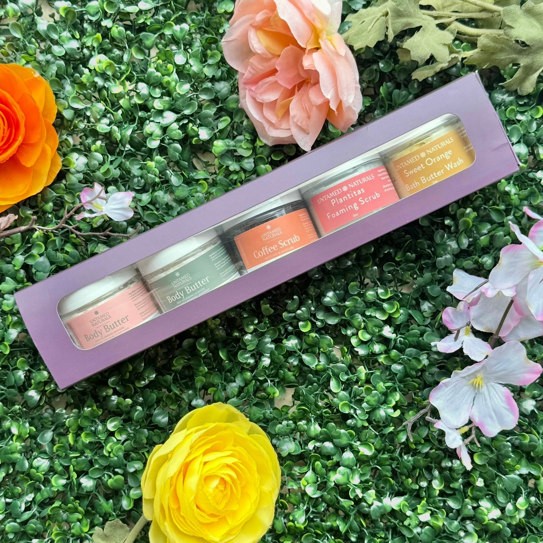 Set of small jars with colorful labels in a purple box on a green grass background with flowers.