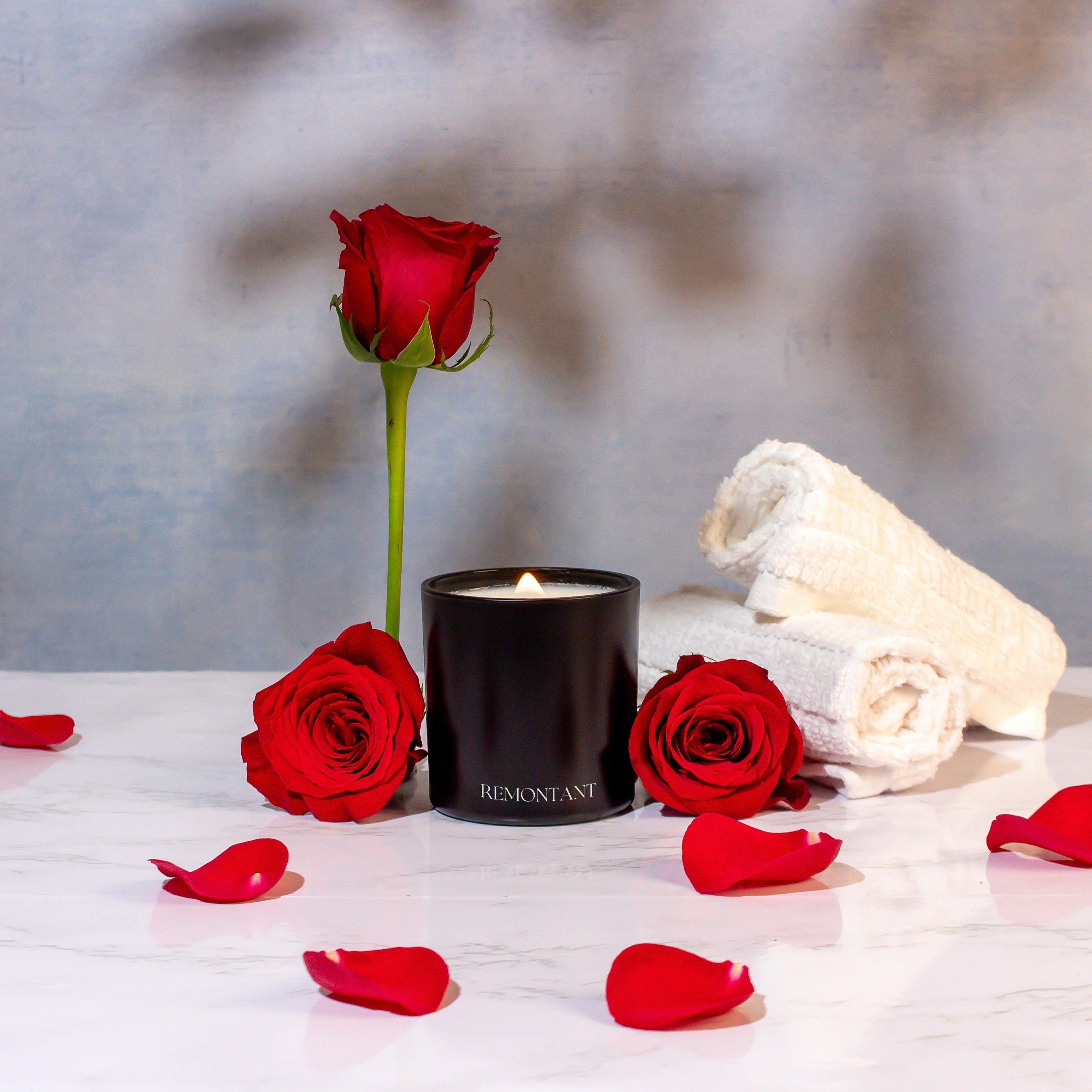 Black candle with red roses and white towels on a light surface