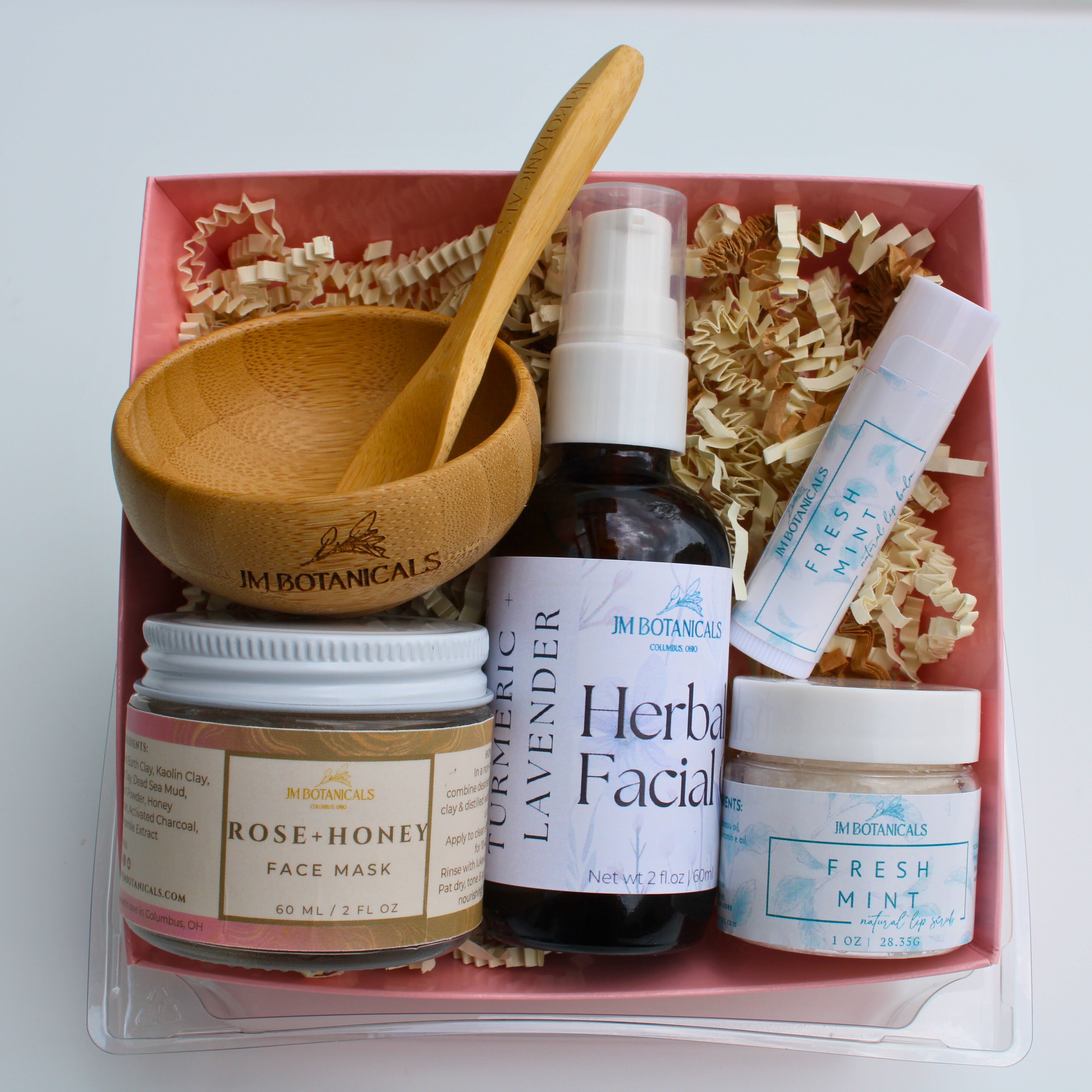 Collection of botanical skincare products in a box with a wooden spoon and shredded paper.