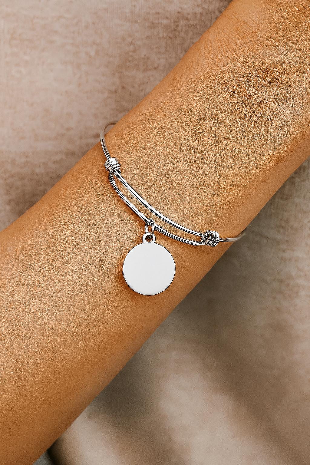 Silver bracelet with a round pendant on a wrist against a beige background