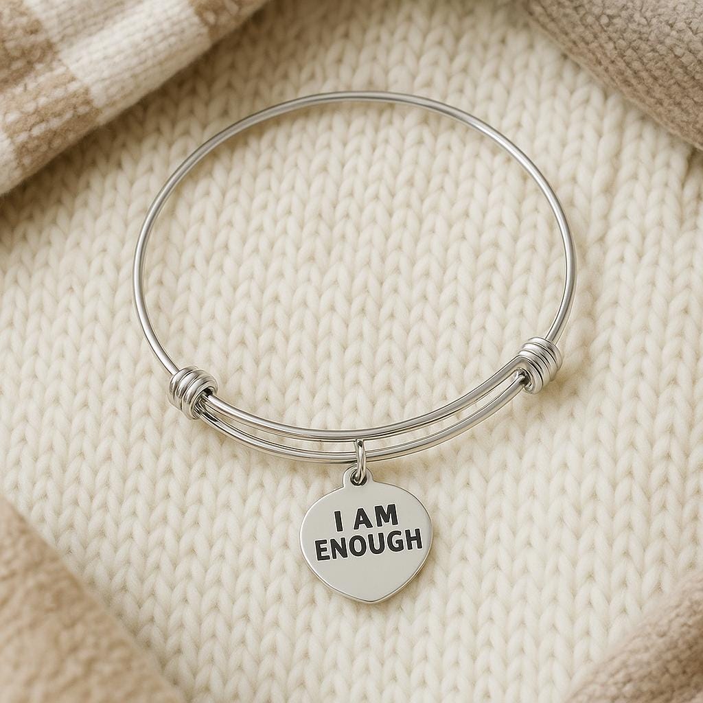 Silver bangle with 'I AM ENOUGH' charm on a beige fabric background